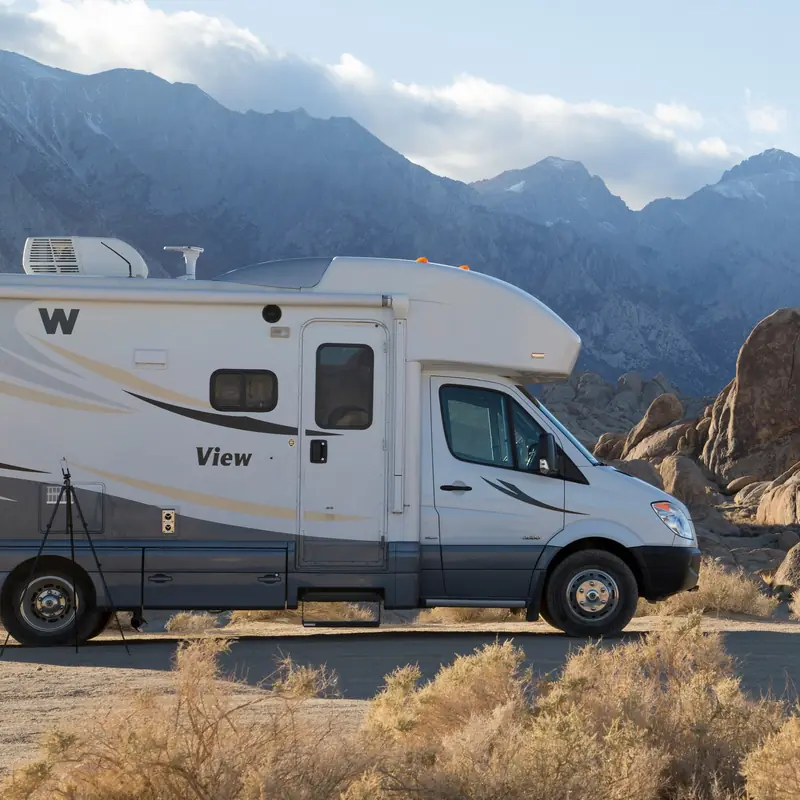Autocaravana capuchina blanca aparcada entre rocas, con la sierra al fondo