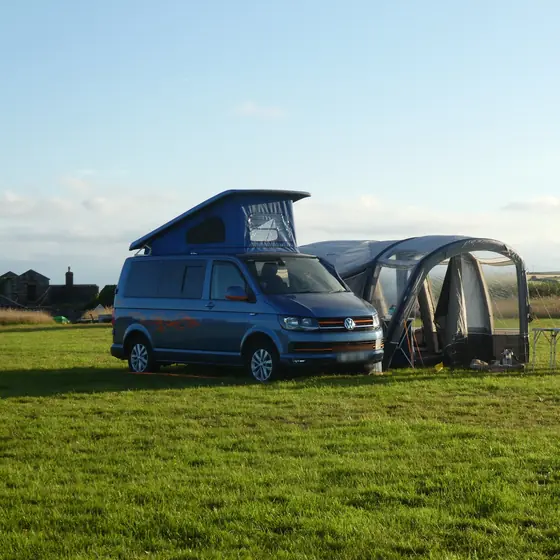 Furgoneta camper azul con el techo elevable y un avance hinchable en un prado