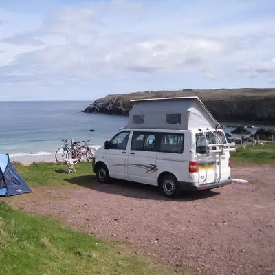 Furgoneta camper blanca con techo elevable y bicis en un camping junto a la playa