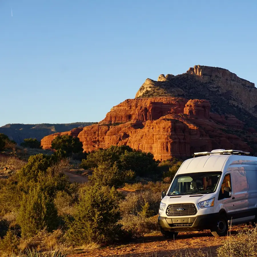 Furgoneta camper blanca aparcada entre rocas rojas al atardecer