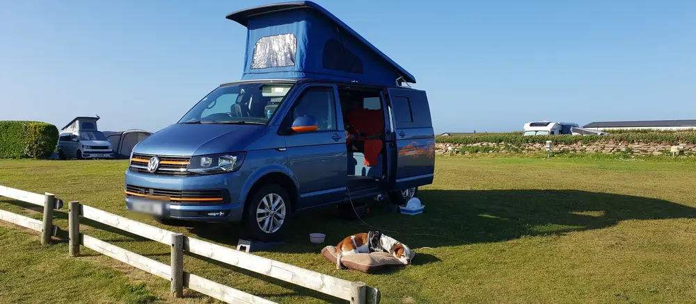 Furgoneta camper azul con el techo elevable abierto en una pradera junto al mar