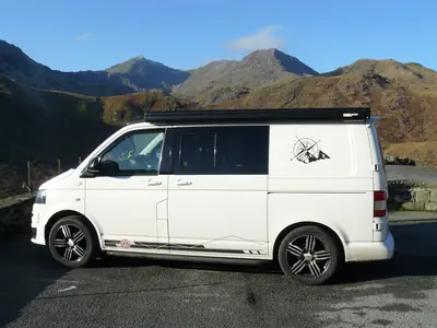 Furgoneta camper blanca de perfil con montañas detrás