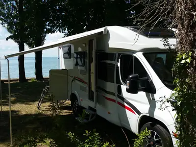 Autocaravana perfilada con el toldo desplegado a la sombra, junto a un lago